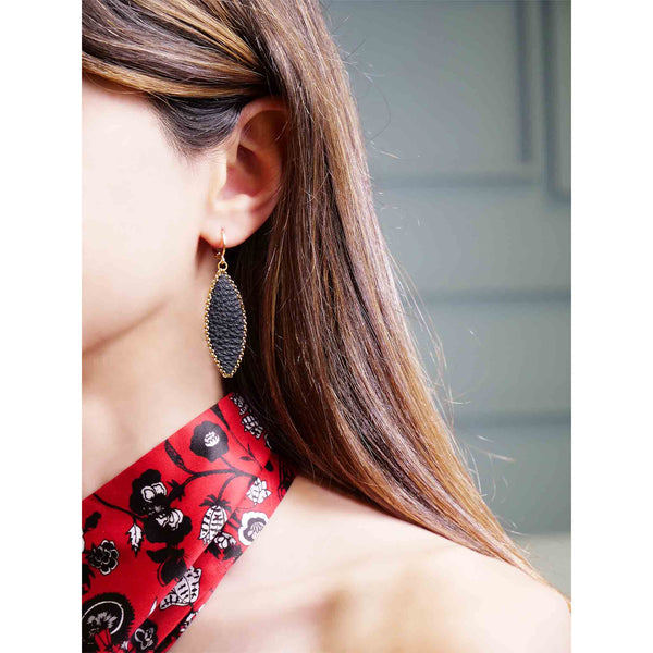 Boucle d'oreille pendante Nune modèle Auris en forme d'épi en cuir noir grainé cerclé de chaîne dorée, portée à l'oreille