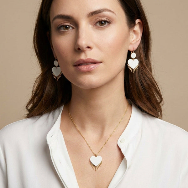 Collier doré Vénus en forme de cœur style ex-voto en cuir recyclé blanc satiné, et les boucles d'oreilles Venus assorties, portés par une femme brune