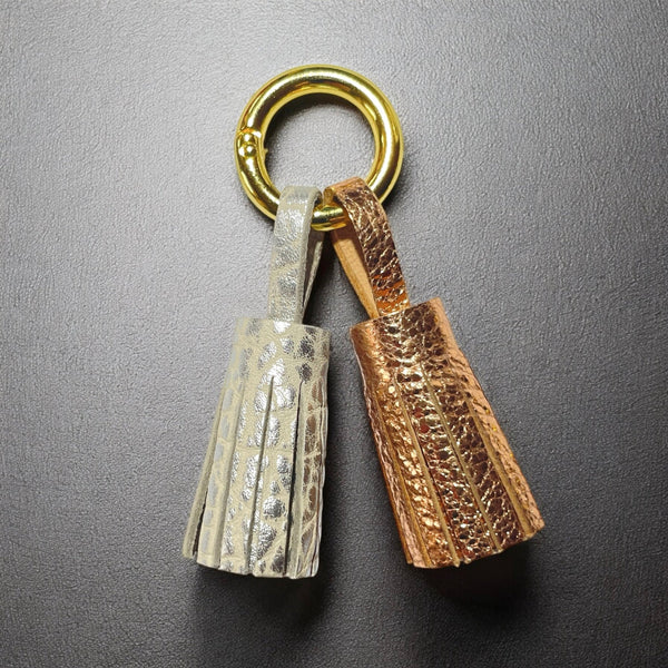 Bijou de sac doré avec 2 pompons en cuirs argent grainé et or rosé froissé, sur fond noir