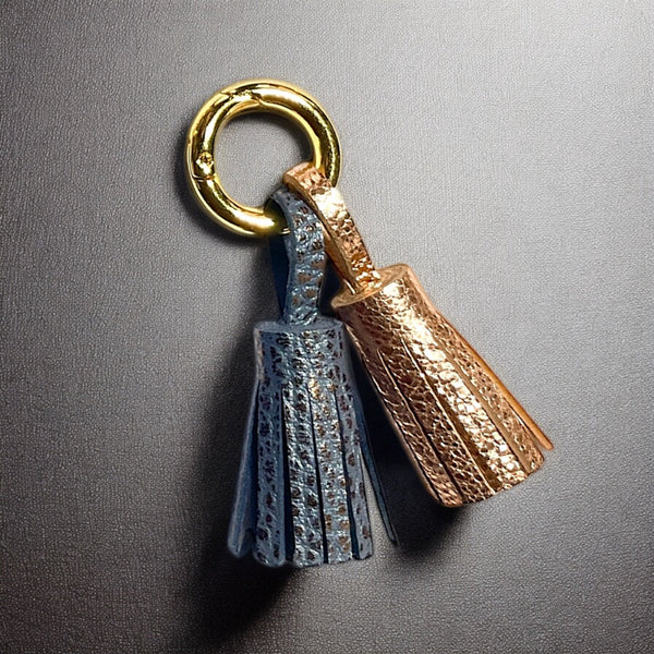 Bijou de sac doré avec 2 pompons en cuirs gris mordoré grainé et or rosé froissé, sur fond noir