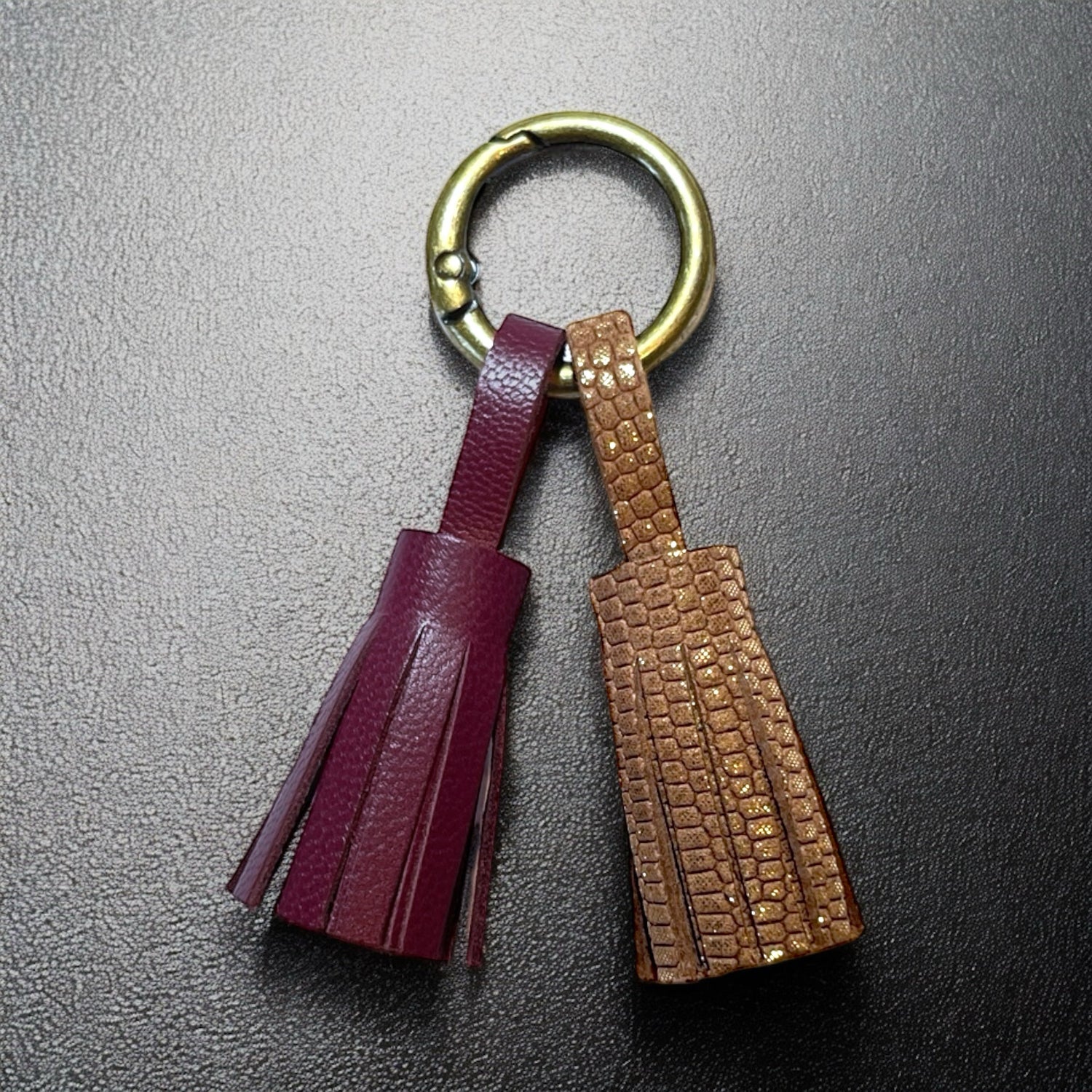 Bijou de sac bronze avec 2 pompons en cuirs pourpre et fauve or façon serpent, sur fond noir