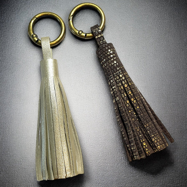 2 Bijoux de sac bronze, chacun portant un grand pompon en cuirs doré clair nacré et brun or façon serpent, sur fond noir