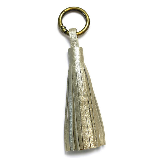 Bijou de sac bronze,  portant un grand pompon en cuir doré clair nacré, sur fond blanc