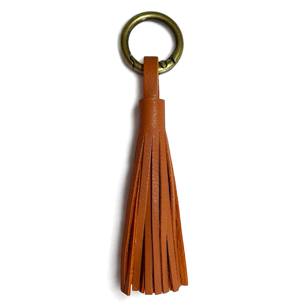Bijou de sac bronze,  portant un grand pompon en cuir terracotta, sur fond blanc