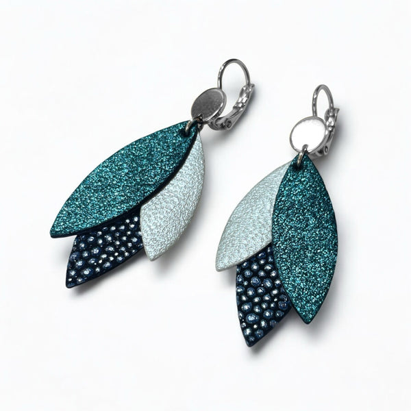 Boucles d'oreilles pendantes argentées et plumes de cuir dans les tons bleutés, sur fond blanc