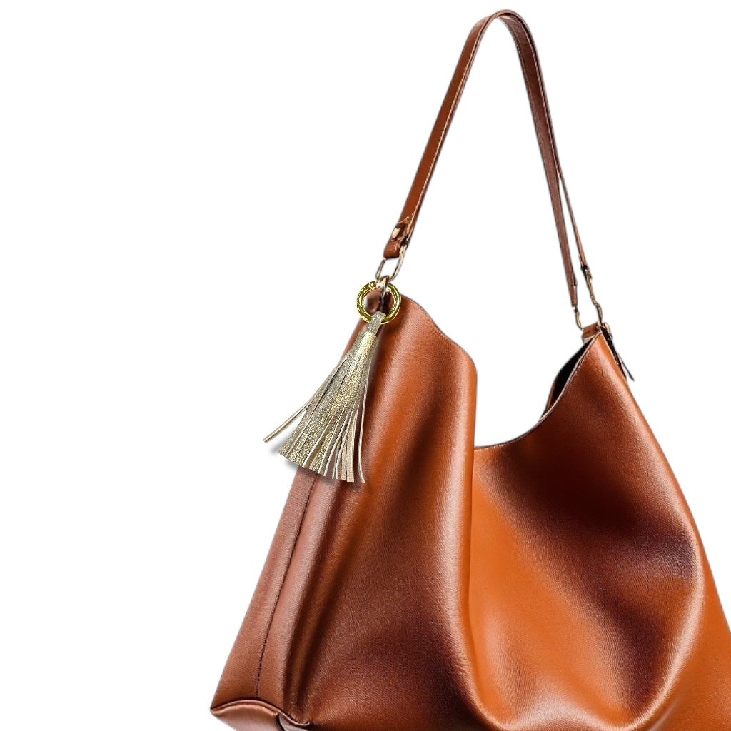 Bijou de sac doré portant un grand pompon en cuir doré vintage , sur un sac en cuir terracotta