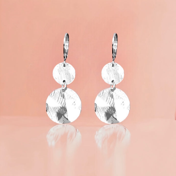 Petites boucles d'oreilles argentées pendantes avec 2 petits sequins ronds en métal martelé, sur fond rosé