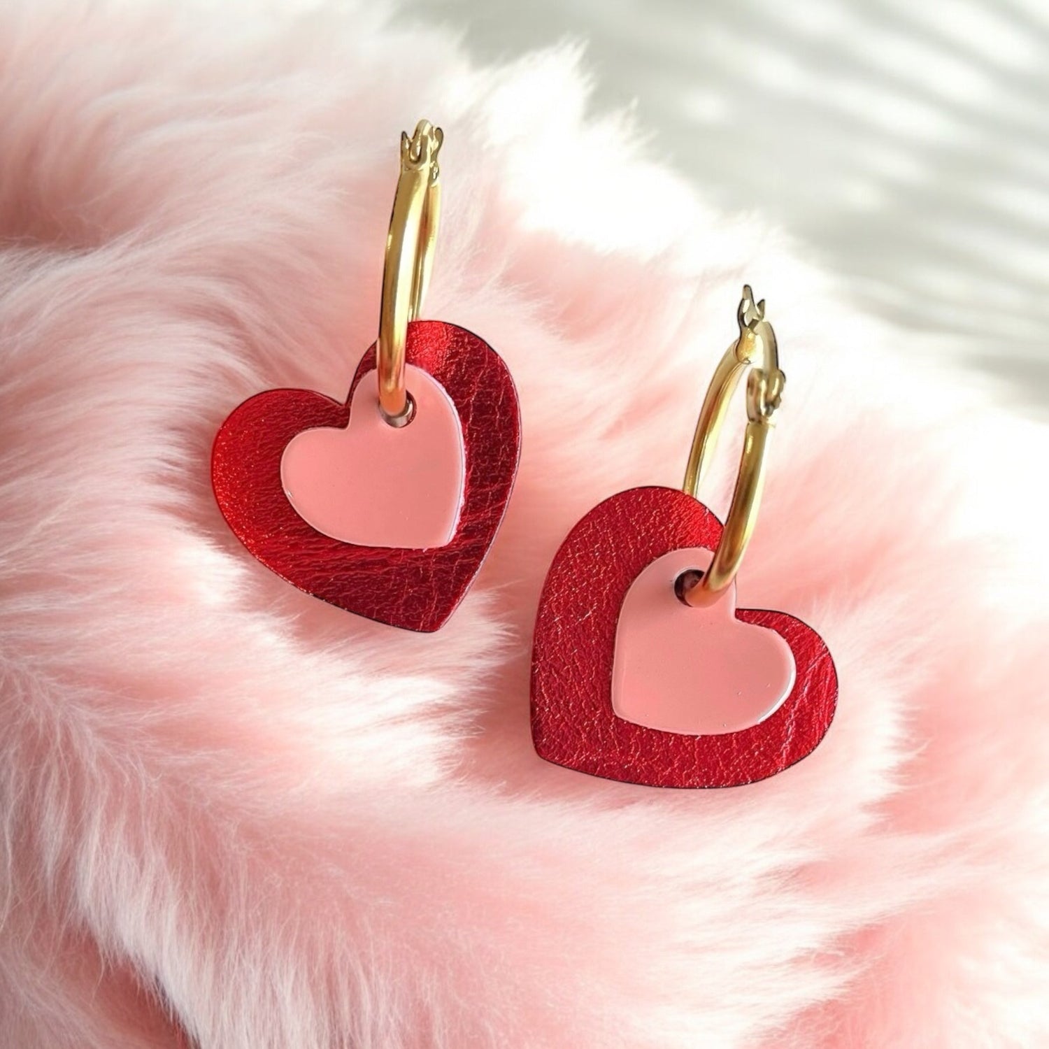 Boucles créoles dorées avec pendentifs en forme de cœurs rouge métallisé et rose vernis, sur fourrure rose pastel