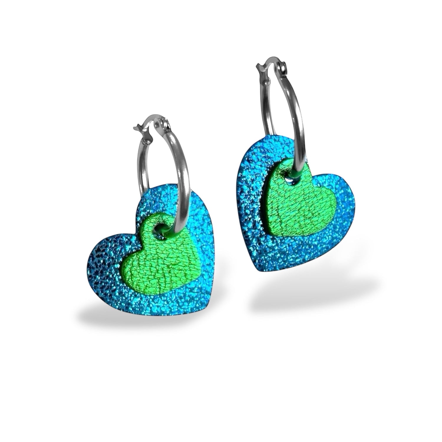 Boucles créoles argentées avec pendentifs en forme de cœurs bleu roi métallisé et vert métallisé, debout sur fond blanc 