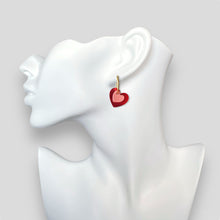 Charger l&#39;image dans la galerie, Boucles créoles dorées avec pendentifs en forme de cœurs rouge métallisé et rose vernis, portées à l&#39;oreille sur un buste blanc
