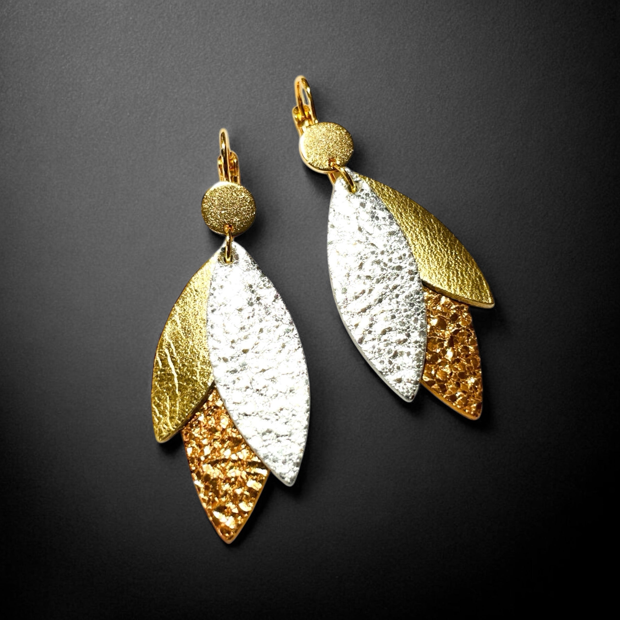 Boucles d'oreilles modèle Ombline de la marque Nune, avec dormeuses dorées et pétales de cuirs trois Ors sur fond noir