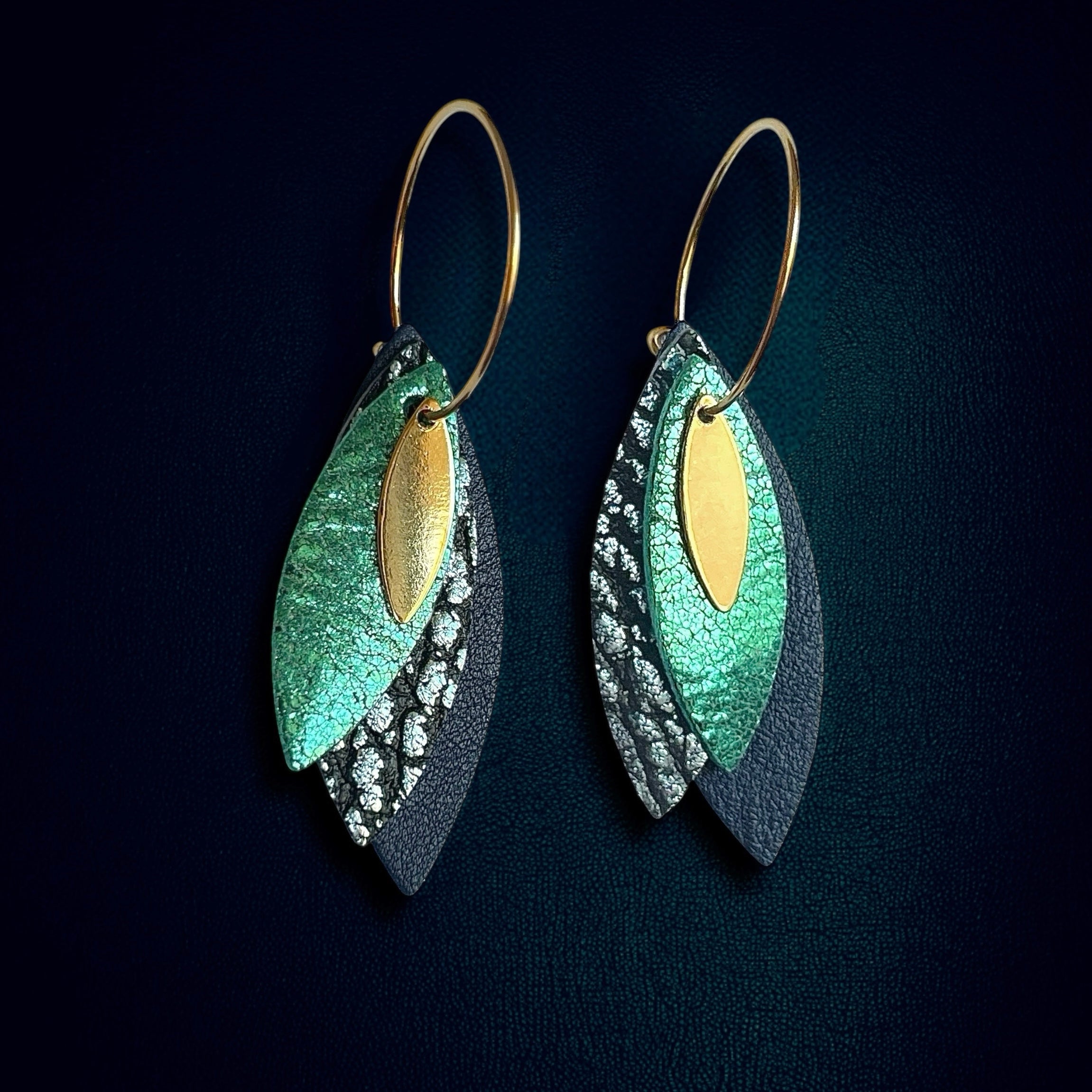 Boucles d'oreilles créoles dorées Nune modèle Piume en cuirs émeraude, bleu glacier métallisé et bleu marine, sur fond bleu nuit