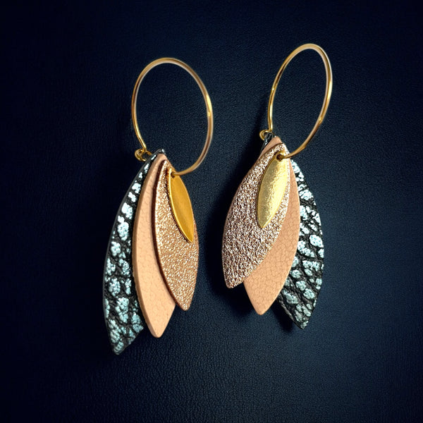 Boucles d'oreilles créoles dorées Nune modèle Piume en cuirs cannelle dorée, rose pâle et bleu glacier métallisé grainé, sur fond bleu nuit