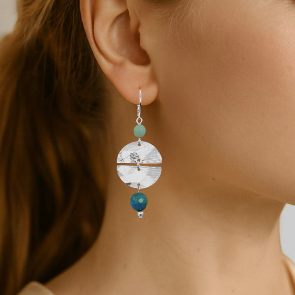 Boucles d'oreilles pendantes de forme ronde avec 2 demi-lunes, en métal martelé argenté et perles d'amazonite et d'apatite bleue, portées à l'oreille