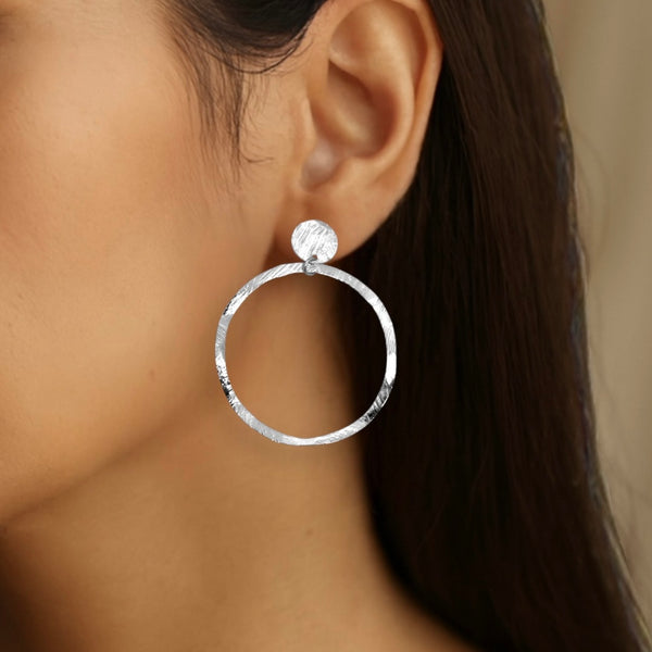 Grandes boucles d'oreilles créoles argentées en métal martelé, montées sur puces rondes, portées aux oreilles 