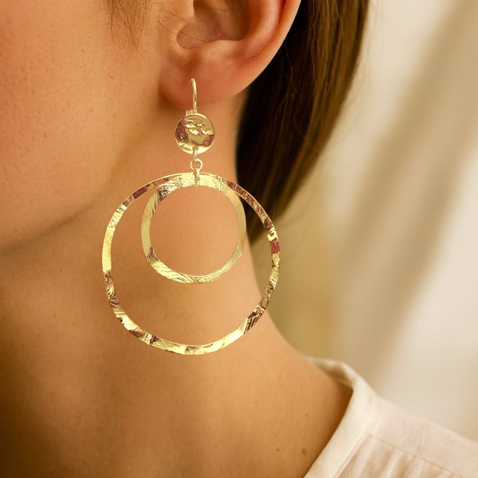 Grandes boucles d'oreilles créoles dorées à double anneau en métal martelé, avec attaches-dormeuses, portées aux oreilles