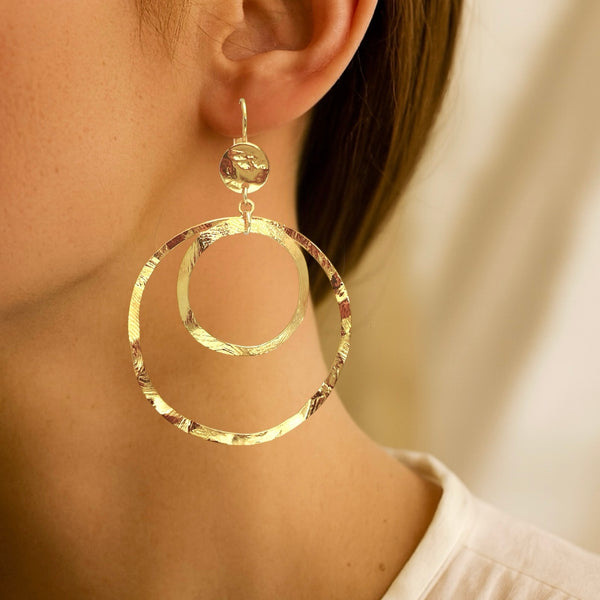 Grandes boucles d'oreilles créoles dorées à double anneau en métal martelé, avec attaches-dormeuses, portées aux oreilles