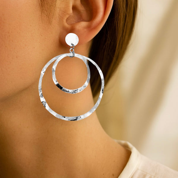Grandes boucles d'oreilles créoles argentées à double anneau en métal martelé, montées sur puces, portées aux oreilles