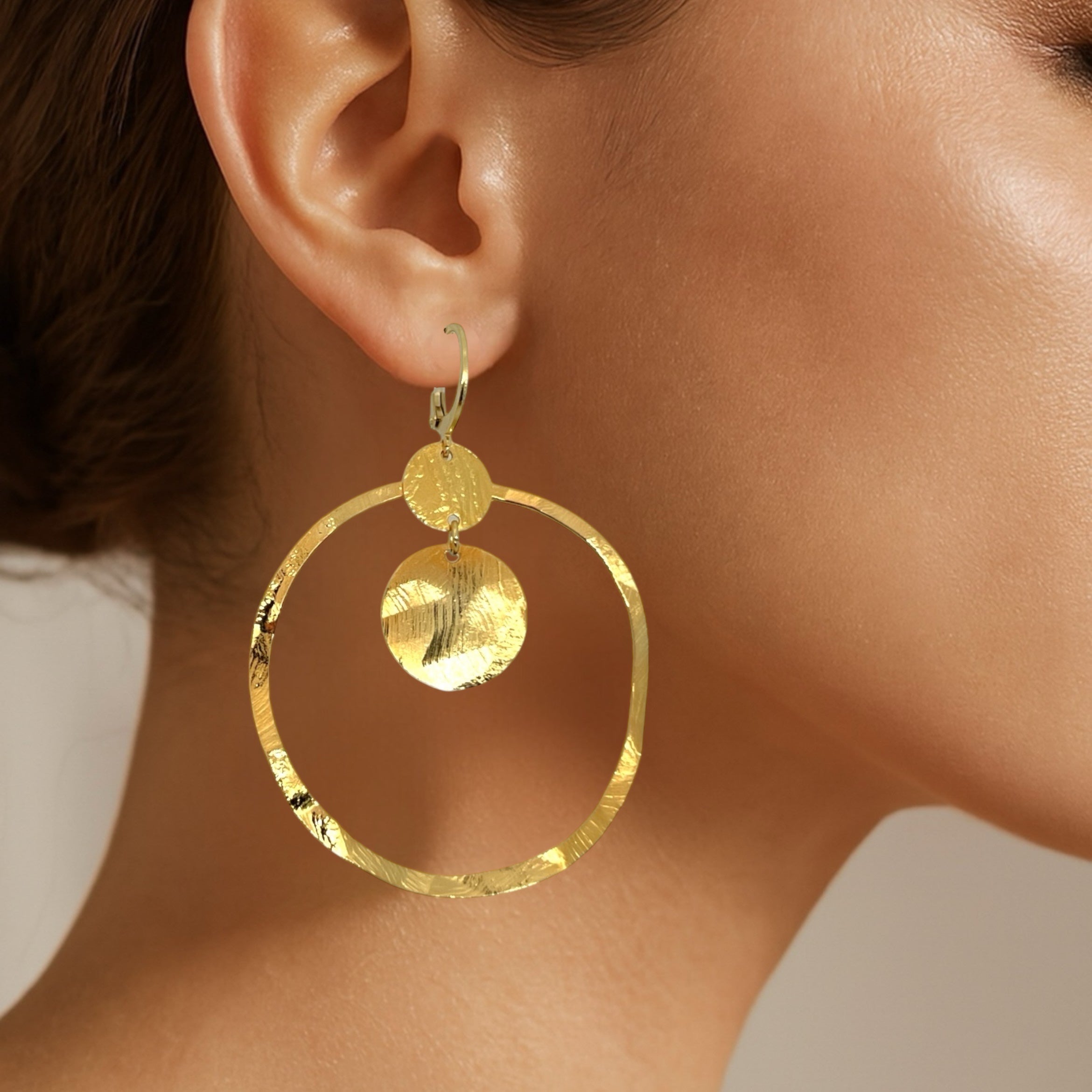 Grandes boucles d'oreilles créoles dorées avec sequins en métal martelé, avec attaches-dormeuses, portées aux oreilles