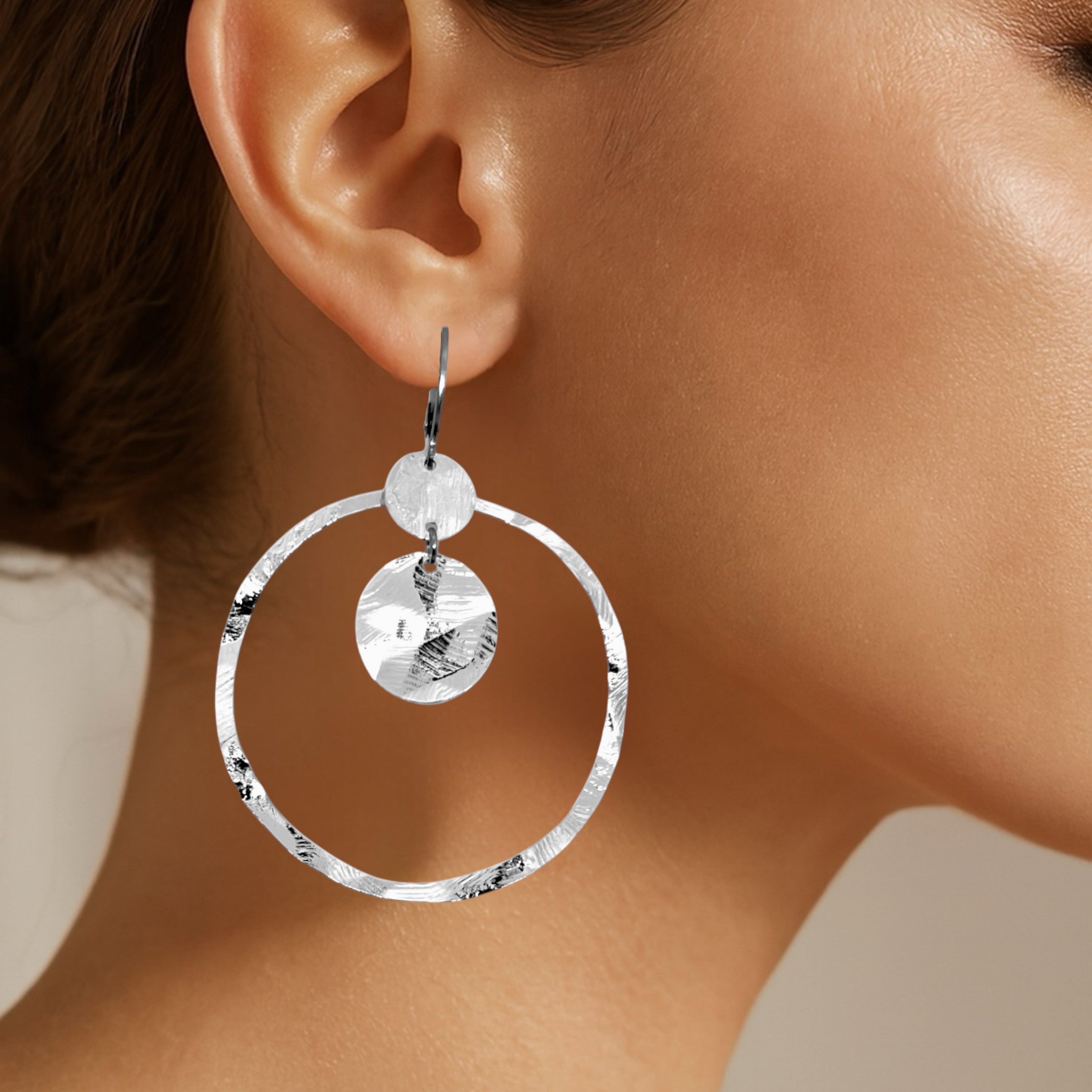 Grandes boucles d'oreilles créoles argentées avec sequins en métal martelé, avec attaches-dormeuses, portées aux oreilles