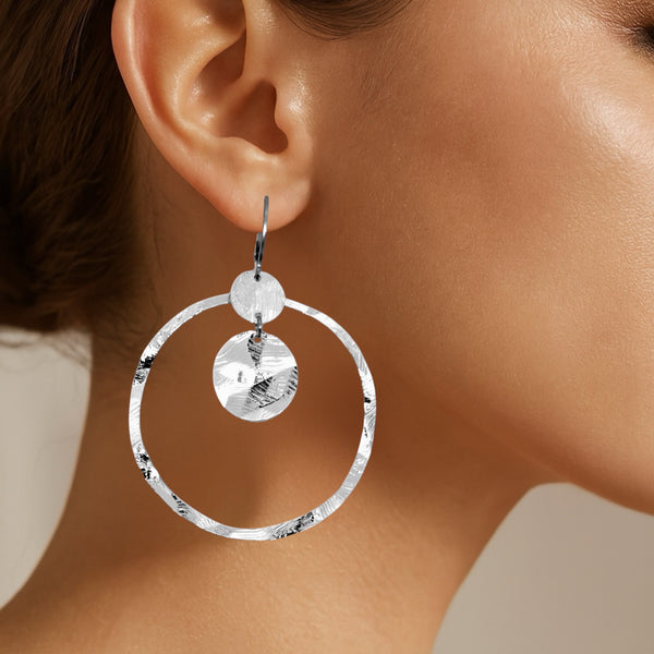 Grandes boucles d'oreilles créoles argentées avec sequins en métal martelé, avec attaches-dormeuses, portées aux oreilles