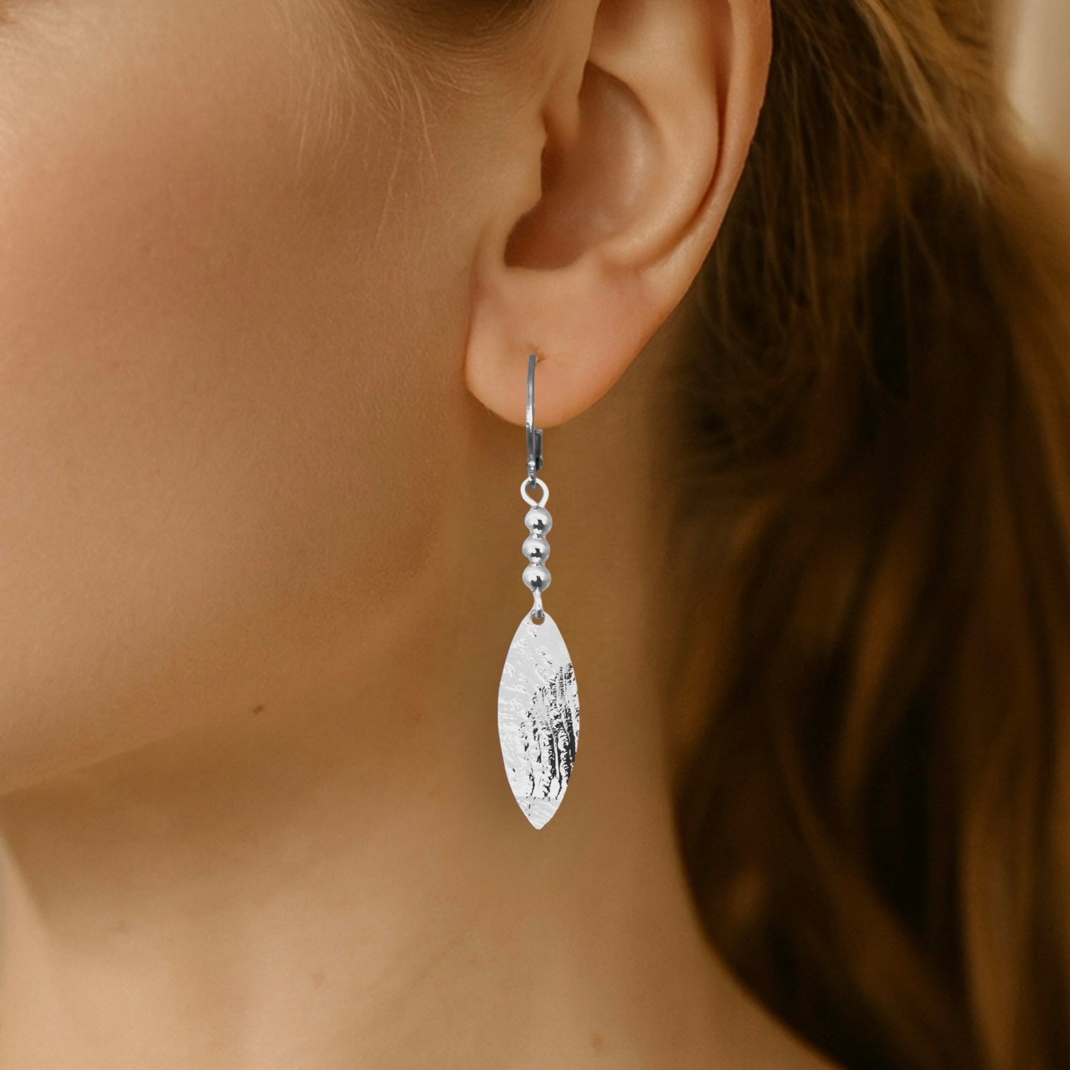 Boucles d'oreilles argentées fines pendantes longues en pointes, portées aux oreilles 