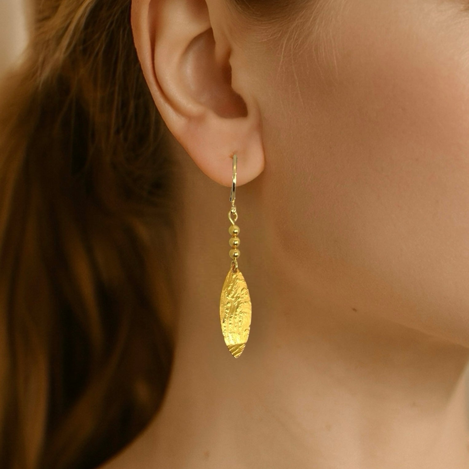 Boucles d'oreilles dorées fines pendantes en pointes, portées aux oreilles