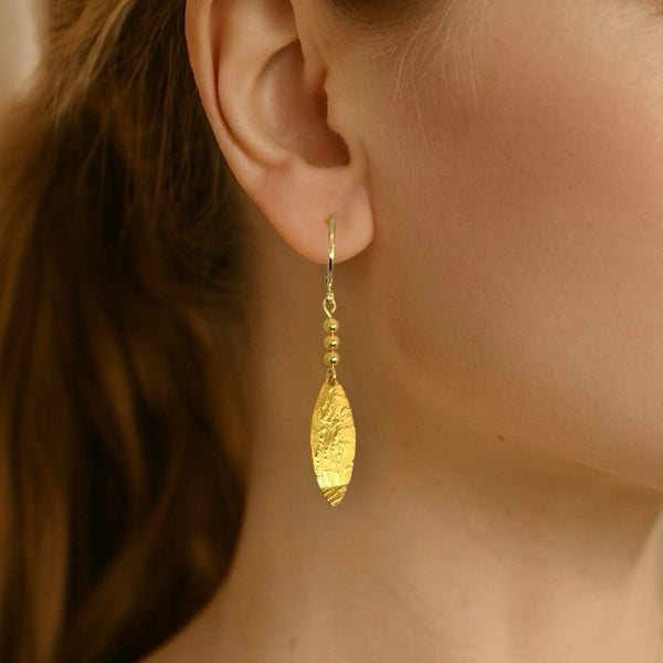 Boucles d'oreilles dorées fines pendantes en pointes, portées aux oreilles