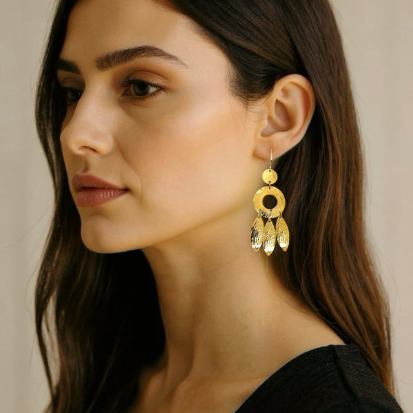 Longues boucles d'oreilles dorées à l'or fin en métal martelé, de style ethnique bohème chic, avec leurs pampilles en forme de plumes, portées aux oreilles