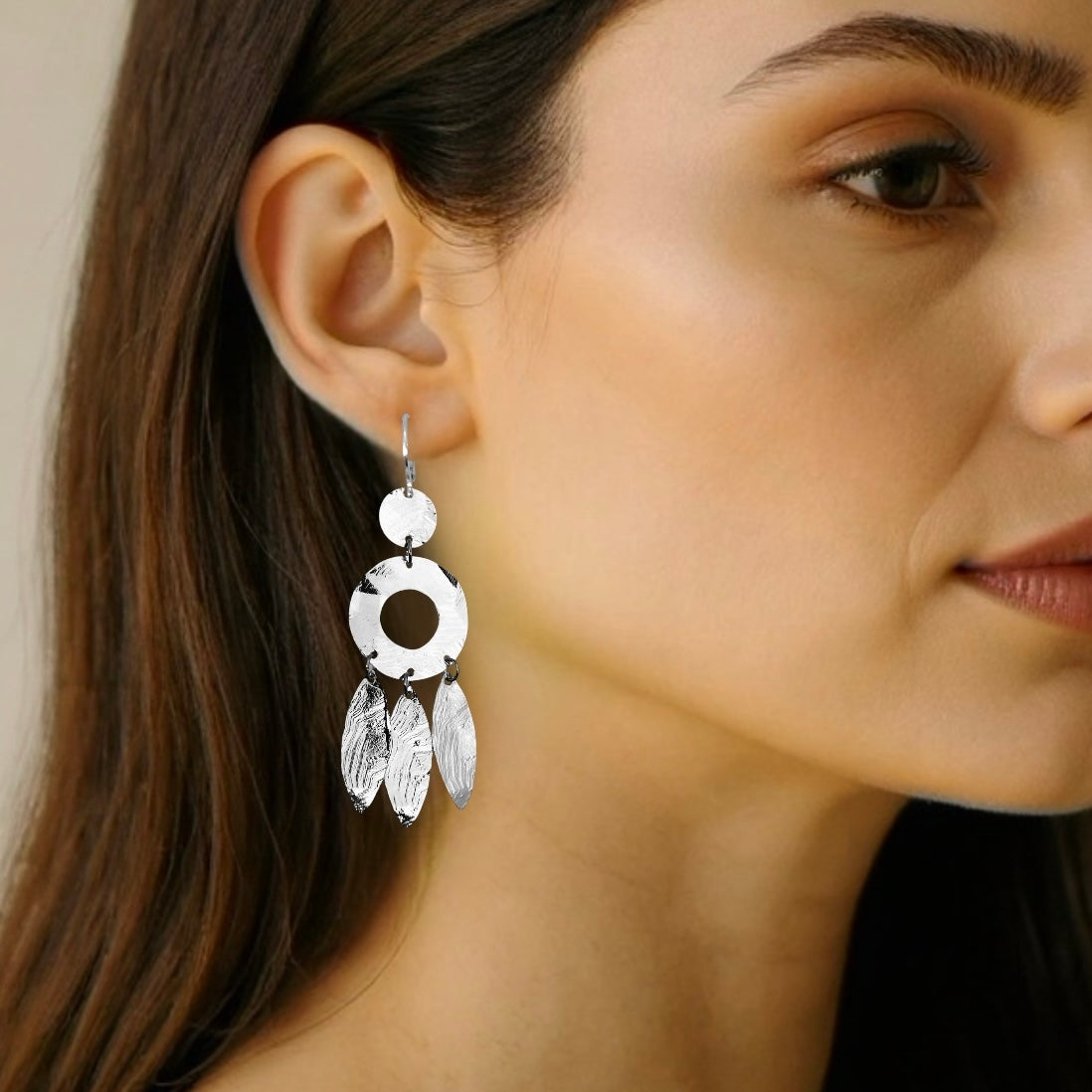 Longues boucles d'oreilles argentées en métal martelé, de style ethnique bohème chic, avec leurs pampilles en forme de plumes, portées aux oreilles 