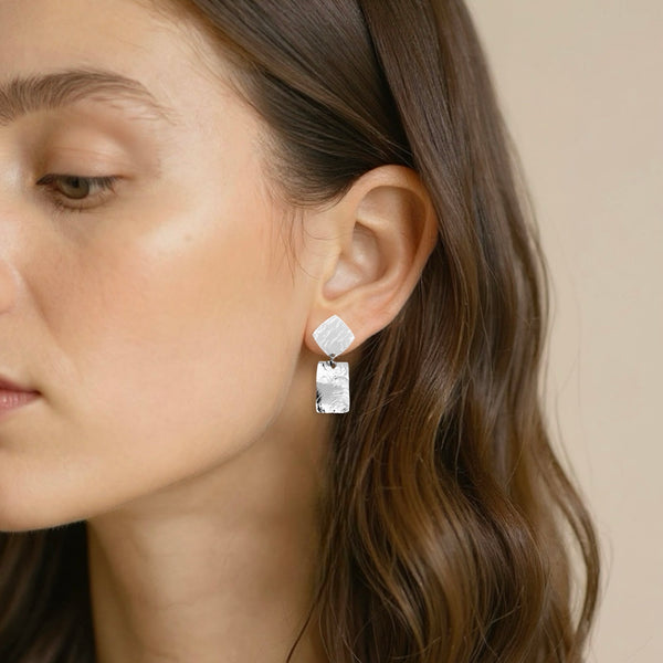 Petites puces d'oreilles losanges avec pendant rectangulaire en métal martelé argenté,  portées aux oreilles