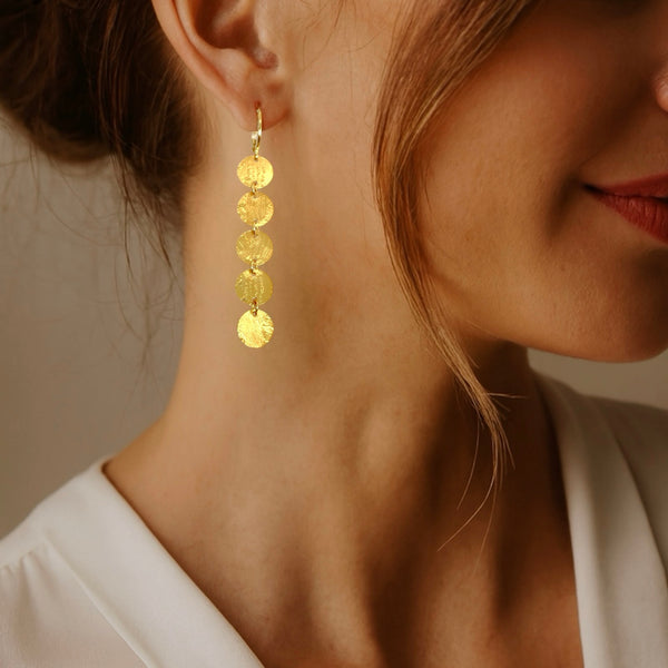 Fines longues boucles d'oreilles dorées pendantes en chapelet de 5 petits sequins ronds, portées aux oreilles