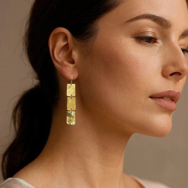 Boucles d'oreilles pendantes en chapelet de 3 rectangles en métal martelé doré à l'or fin, portées aux oreilles