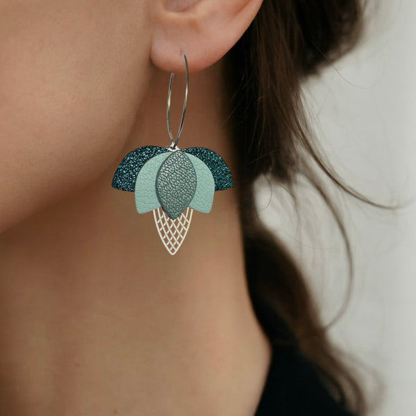 Créoles dorées en forme de fleurs de Lotus en cuirs bleu paon pailleté, bleu nuage et bleu gris nacré portées aux oreilles