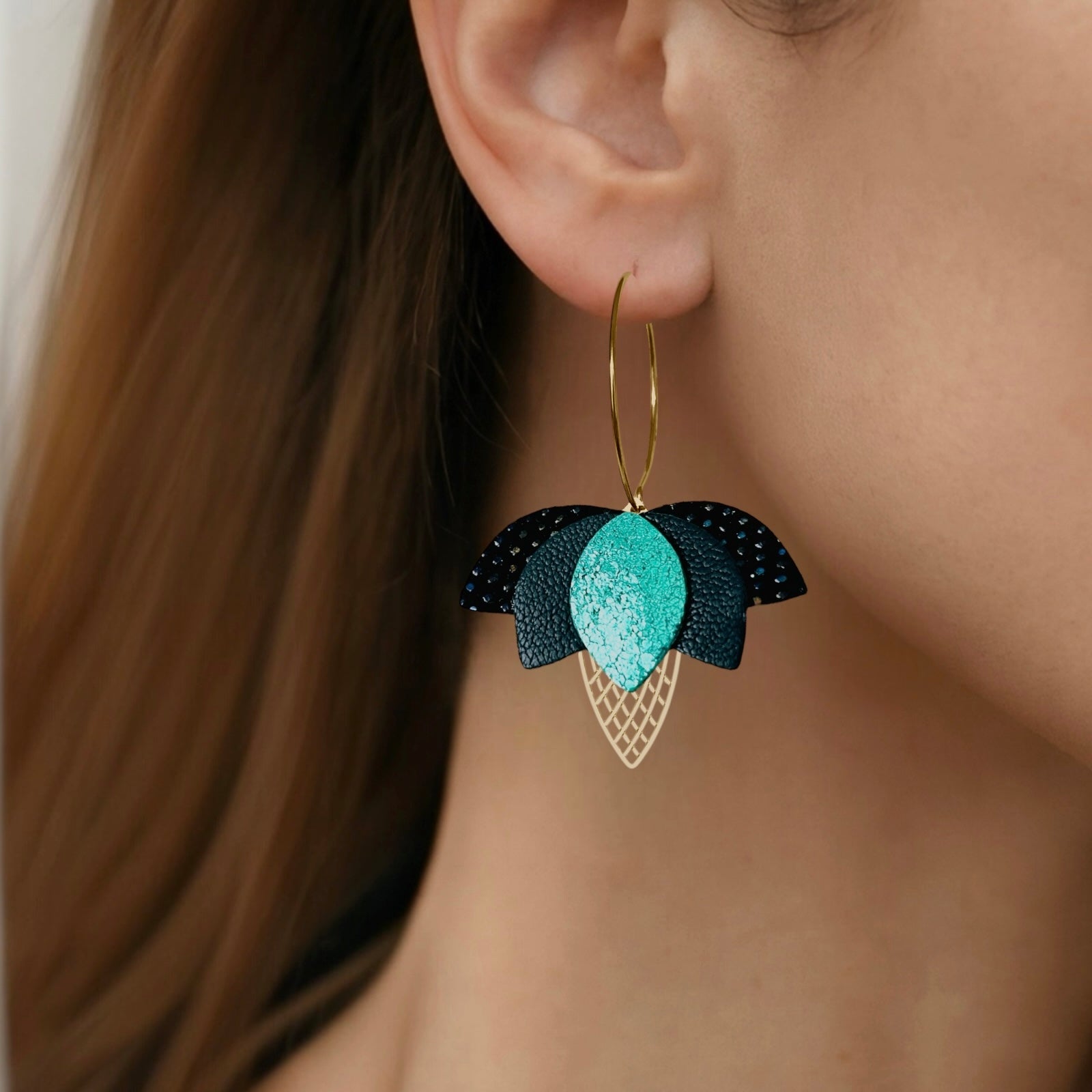 Créoles dorées Nune en forme de fleurs de Lotus en cuirs noir grainé irisé, vert sombre et vert émeraude brillant intense portées à l'oreille