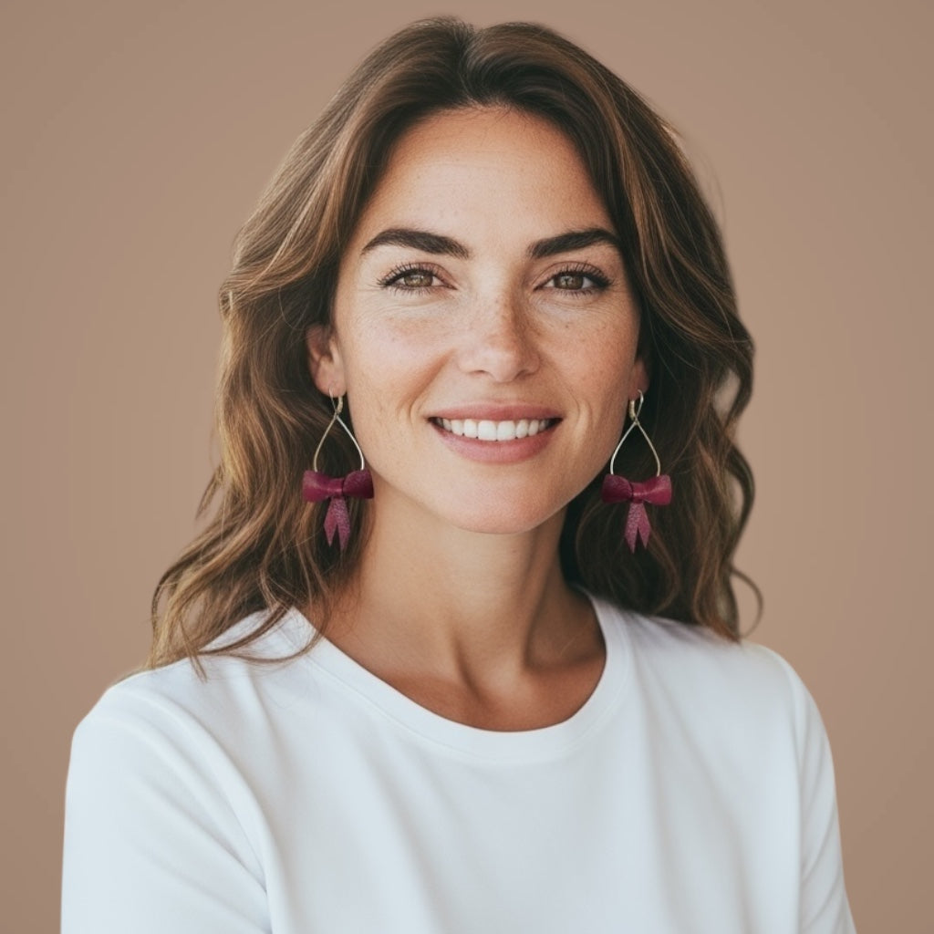 Boucles d'oreilles dorées pendantes et légères en forme de gouttes, décorées de délicats nœuds de rubans de cuir pourpre, portées aux oreilles