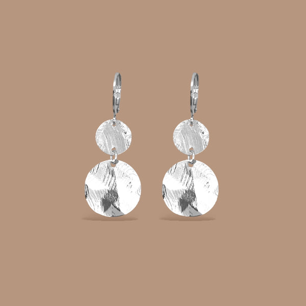 Petites boucles d'oreilles argentées pendantes avec 2 petits sequins ronds en métal martelé, sur fond beige