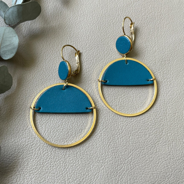 Paire de boucles d'oreilles créoles dorées Nune modèle Lua avec cuir vert canard, sur fond cuir beige doré