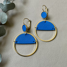 Charger l&#39;image dans la galerie, Paire de boucles d&#39;oreilles créoles dorées Nune modèle Lua avec cuir bleu roi, sur fond cuir beige doré
