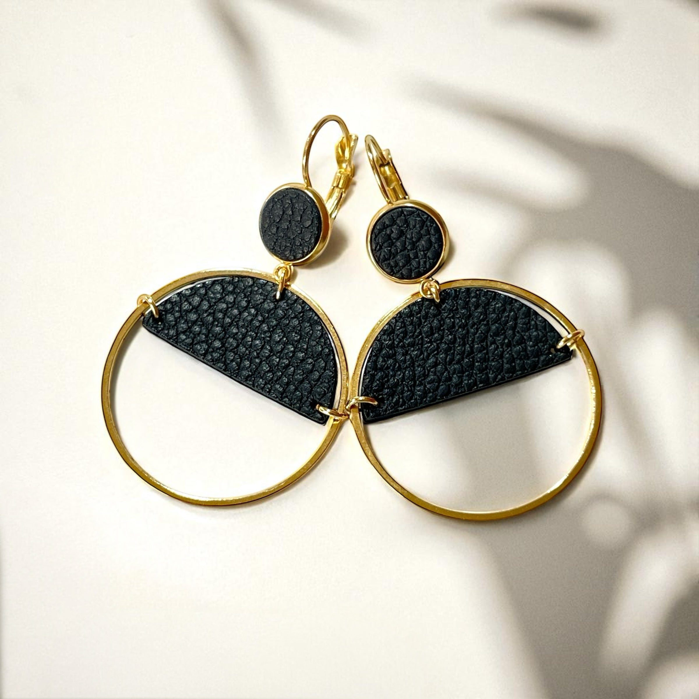 Paire de boucles d'oreilles créoles dorées Nune modèle Lua avec cuir noir grainé, sur fond cuir beige doré