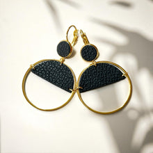 Charger l&#39;image dans la galerie, Paire de boucles d&#39;oreilles créoles dorées Nune modèle Lua avec cuir noir grainé, sur fond cuir beige doré
