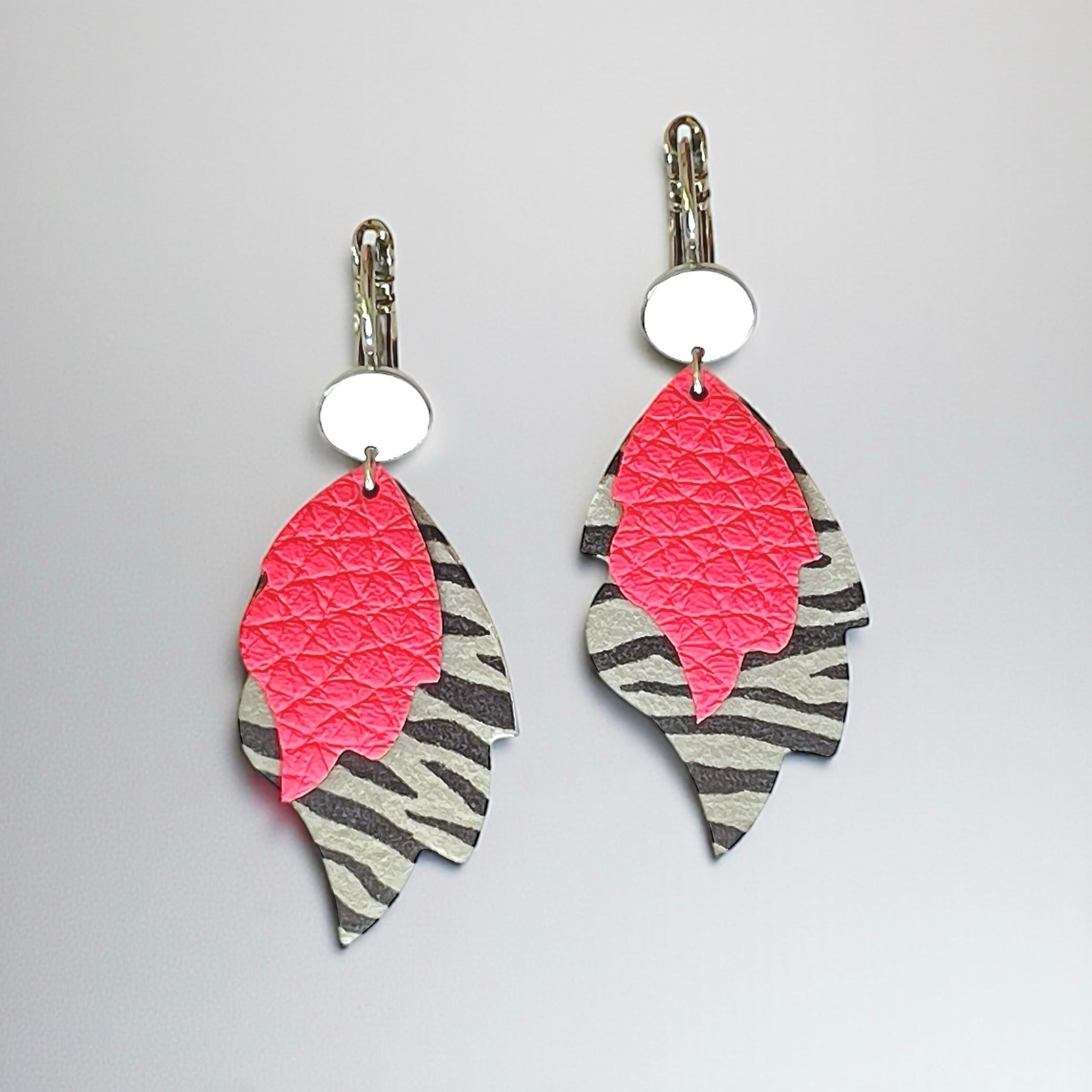 Boucles d'oreilles argentées bohème-chics en forme de flammes en cuir rose fluo grainé et cuir zébré noir, sur fond gris