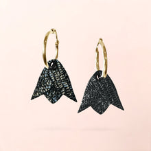 Charger l&#39;image dans la galerie, Boucles d&#39;oreilles créoles dorées avec pendentifs légers en cuir noir brillant façon serpent en forme de tulipe, sur fond rose pâle
