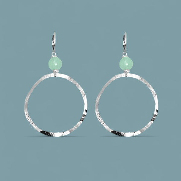 Boucles d'oreilles créoles de forme ronde en métal martelé argenté et perles de fluorite vert d'eau, sur fond bleu gris