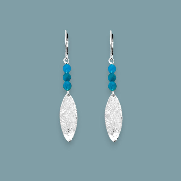 Boucles d'oreilles fines en pointe en métal martelé doré à l'or fin et petites perles d'apatite bleue, sur fond bleu gris