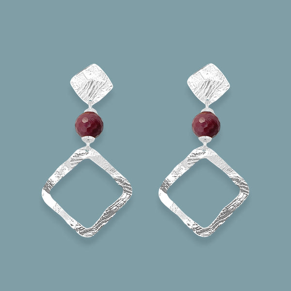 Boucles d'oreilles losanges sur puces en métal martelé argenté et perles de Mokaïte bordeaux, sur fond bleu gris
