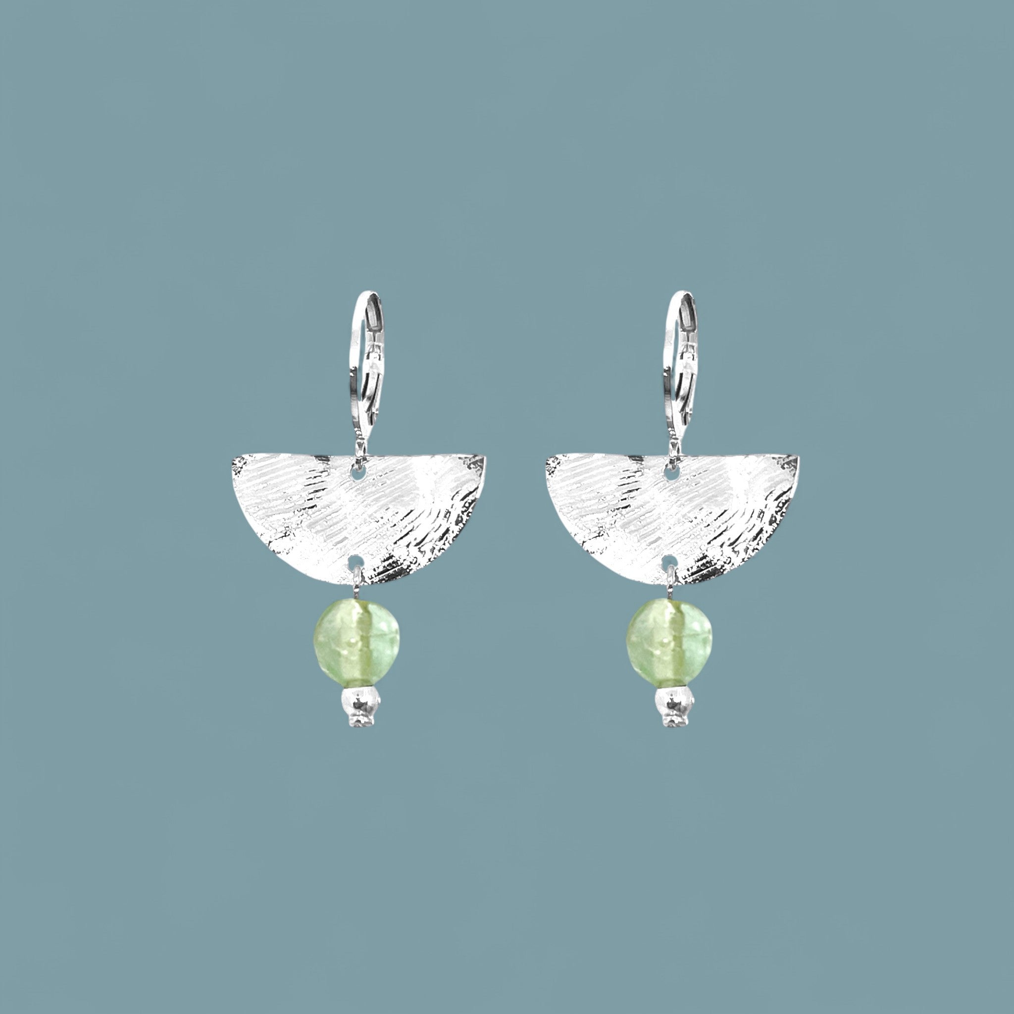 Petites boucles d'oreilles pendantes, de forme demi-lune, en métal martelé argenté et perles de fluorite vert d'eau, sur fond bleu gris