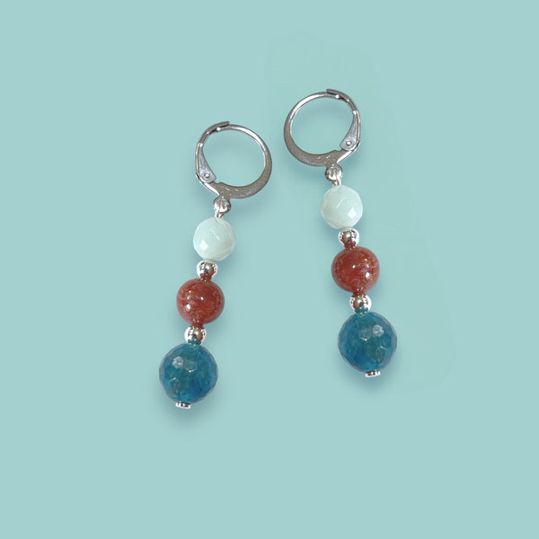 Boucles d'oreilles pendantes argentées en perles de pierres naturelles colorées dans les tons bleu et brique sur fond vert pastel