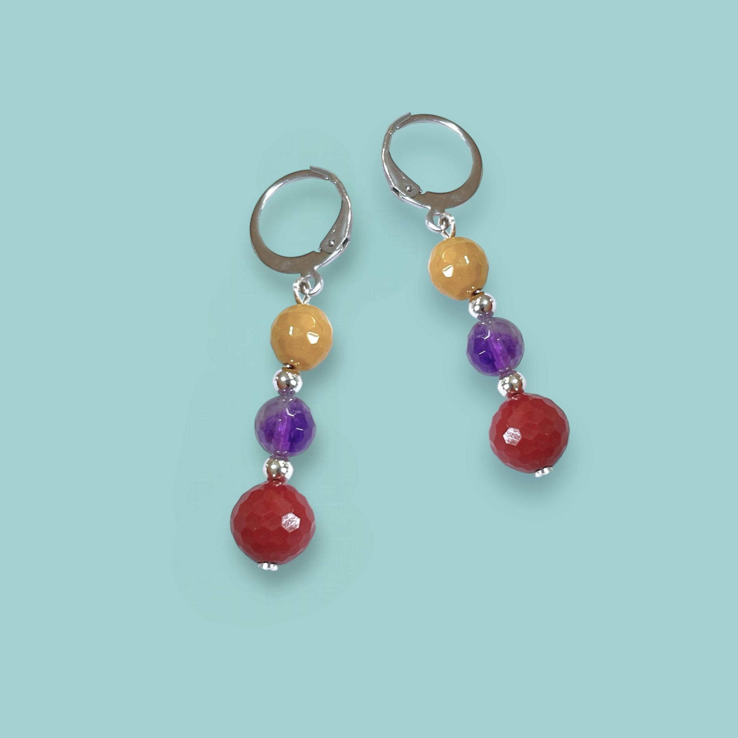 Boucles d'oreilles pendantes argentées en perles de pierres naturelles colorées sur fond vert pastel