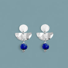 Charger l&#39;image dans la galerie, Boucles d&#39;oreilles puces pendantes de forme demi-lune, en métal martelé argenté et perles de Lapis Lazuli, sur fond bleu gris

